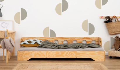 Drewniane łóżko z barierką o okrągłych wycięciach na długim boku wykonane ze sklejki sosnowej w kolorze lakierowanego drewna